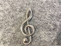 Front view of the treble clef sterling silver brooch showing polished surface and rounded shape.