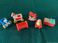 Seven colorful plastic vintage Fisher Price nursery toys displayed on green fabric.