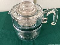 Full view of Pyrex coffee percolator showing glass body, metal basket inside, glass lid with knob, and handle.