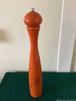 Full front view of tall orange pepper grinder with silver top knob and Mario Batali signature at the base.