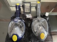 Two full face snorkeling masks (blue and gray) laid flat with breathing tubes and mesh storage bags, also showing a transparent waterproof mobile phone dry bag and mounting accessories.