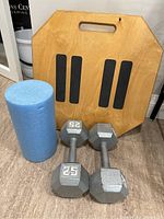 Full view showing wooden balance board, blue foam roller, and two 25lb dumbbells arranged on floor