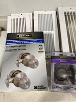 Photo of new Defiant Saturn Collection door knobs in box with white vent covers behind