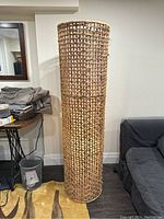 Full view of the tall woven floor lamp, unlit, showing the intricate grid pattern of the natural woven material.