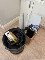 Overview of black plastic nursery pots nested inside each other, gardening accessories such as seed starter kit visible inside top pot, in front of white cabinetry on floor.
