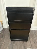 Front view of black metal file cabinet showing five horizontal handles and lock with key at top right corner.