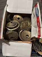 Open box showing coils of gold finish nails for framing