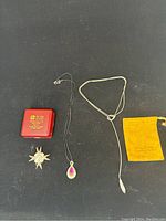 Full lot overview on black background showing red box, Maltese cross pendant, black cord pendant, and silver necklace.