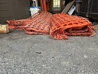 Rolled orange plastic snow fencing laid out on a concrete floor, showing its distinctive open pattern and flexible material.