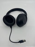 Sony WH-CH710N black wireless headphones lying flat showing USB charging cable attached to left ear cup.