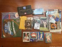 Wide layout image showing various baseball cards including fleer box, assorted packs, and loose cards in sleeves and multiple sealed packs laid out.