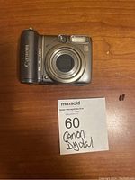 Front view of Canon PowerShot A590 digital camera on wood surface with maxsold auction tag