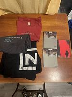 Overview of three folded T-shirts and three DVDs on wooden table.