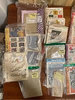 Top-down photo of assorted vintage embroidery transfer packets and patterns from McCall, Simplicity, Butterick stacked and overlapping on tabletop.
