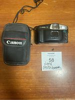 Photo showing vintage Canon Automatic camera with built-in flash, shutter, and viewfinder, positioned next to the Canon carrying case and a lot card.