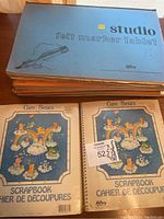 Stack of scrapbooks with a blue cover scrapbook titled 'studio felt marker tablet' and two Care Bears scrapbooks showing colorful cartoon covers with rainbow and characters.