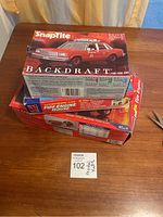 Photo of three vintage Monogram SnapTite model kits stacked on a wooden table, showing the Backdraft 1:32 Fire Car box on top, Fire Engine House box beneath, and another fire engine kit at the bottom.