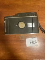 Back and side view of the Polaroid Model 160 Land Camera, laid flat on wooden surface with visible camera body details and attached wrist strap.