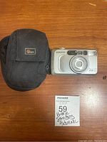 Samsung Maxima Elite 105 camera and black Lowepro carrying case shown on wooden surface with handwritten lot ticket.