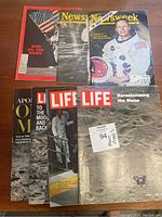 Collection of six vintage magazines and one book all related to the Apollo 11 moon landing, including covers showing astronauts, lunar surface, and iconic images of the mission.