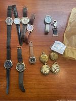 Nine wristwatches and four pocket watches arranged on a wooden surface, showing variety in styles and bands.