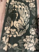 Top view showing the blanket with peacock design and floral border on dark green background.