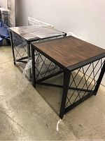 Two matching wood and metal end tables side by side on concrete floor, showing tops and metal criss-cross sides.