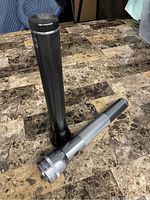 Two flashlights on a tiled surface, one black with textured grip and one silver with smooth handle.