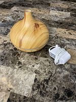 Photo showing the wood grain aromatherapy diffuser and its white power adapter on a marble patterned surface