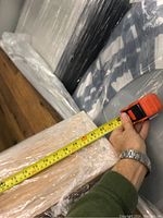 Photo shows tape measure stretched across wooden bed frame piece wrapped in plastic showing length measurement.