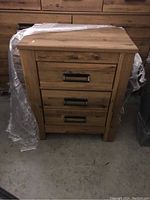 Front view of the wooden bedside table showing three drawers with black metal handles, natural wood grain finish.