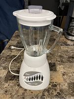 Full front view of the Oster blender showing the glass jar, control panel with buttons, and power cord on a countertop.