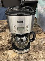 Front view of Sunbeam stainless steel coffee maker showing glass carafe, control panel with buttons and digital display.
