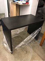 Simple black rectangular desk with solid side panels and matte finish shown in a warehouse setting.