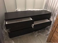 Front view of dark brown dresser with some drawers open, wrapped partially in plastic.