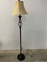 Full view of the black metal floor lamp with beige fabric lampshade standing on the floor.