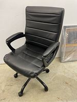 Black office chair with padded backrest, armrests, and five rolling wheels on a black metal base.