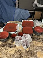 Various angles showing a collection of square plates, bowls, and mugs on a marble table with bubble wrap around some mugs.