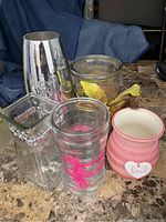 Six assorted decorative vases and a ceramic jar with a heart-shaped 'Loved' tag arranged on a table.