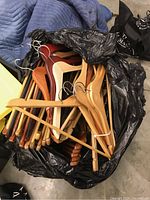 Photo of a black garbage bag filled with assorted wooden coat hangers of various finishes and styles.