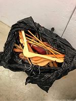 Black garbage bag filled with multiple wooden coat hangers in different shapes and wood tones, seen from above.