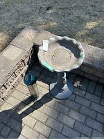 Overall view showing the bird bath and hanging bird feeder side by side outdoors on a paved surface.