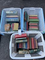 Three plastic bins filled with assorted cloth-bound hardcover books in various colors