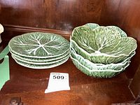 Stack of four cabbage leaf side plates next to four matching cabbage leaf dessert bowls on wooden shelf
