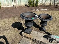 Overview of two cast iron urns outdoors showing overall shape and finish