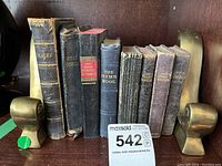 Front view of seven vintage books including Psalms, Holy Bible, Webster's Dictionary, The Hymn Book, two editions of Common Prayer Book, with brass bookends on each end.