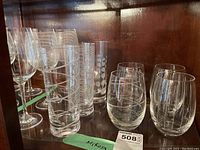 Wide view showing 4 stemless wine glasses and 3 stemmed wine glasses with etched designs along with 3 large glasses on shelf