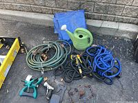 Full view of the garden lot including hoses, tarp, watering can, and hose wall hook.