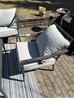 View of the Gluckstein patio chair showing metal frame, armrest, and beige seat and back cushions on a patio surface.