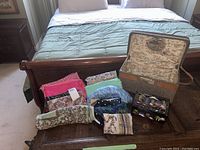 View of all items together on wooden surface: travel cosmetic bag, multiple silk and fabric scarves, Asian-themed jewelry/music box.